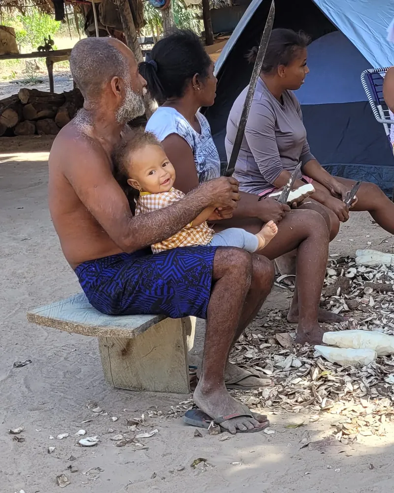 An elder of a Quilombola community in Brazil at work, holding an infant who looks out towards the camera.