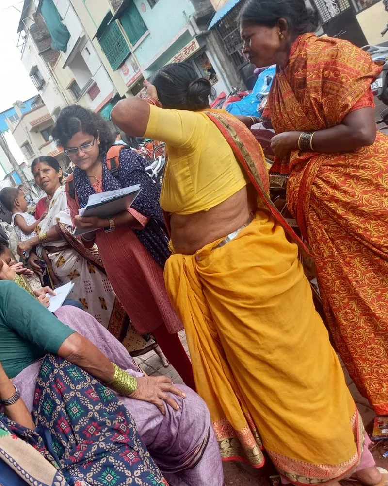 Community women seated with notebooks recording testimony while a colleague stands and speaks.