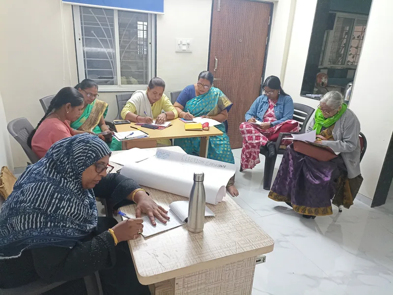 Women sit around tables writing notes, beside a sheet of chart paper headed &ldquo;Election campaign&rdquo;.