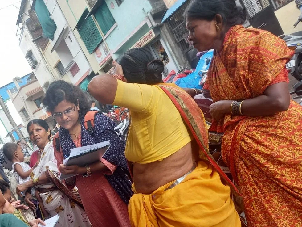 Community women seated with notebooks recording testimony while a colleague stands and speaks.